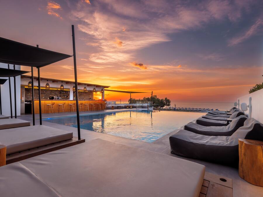 Zona junto a la piscina con sillones de descanso y un bar.