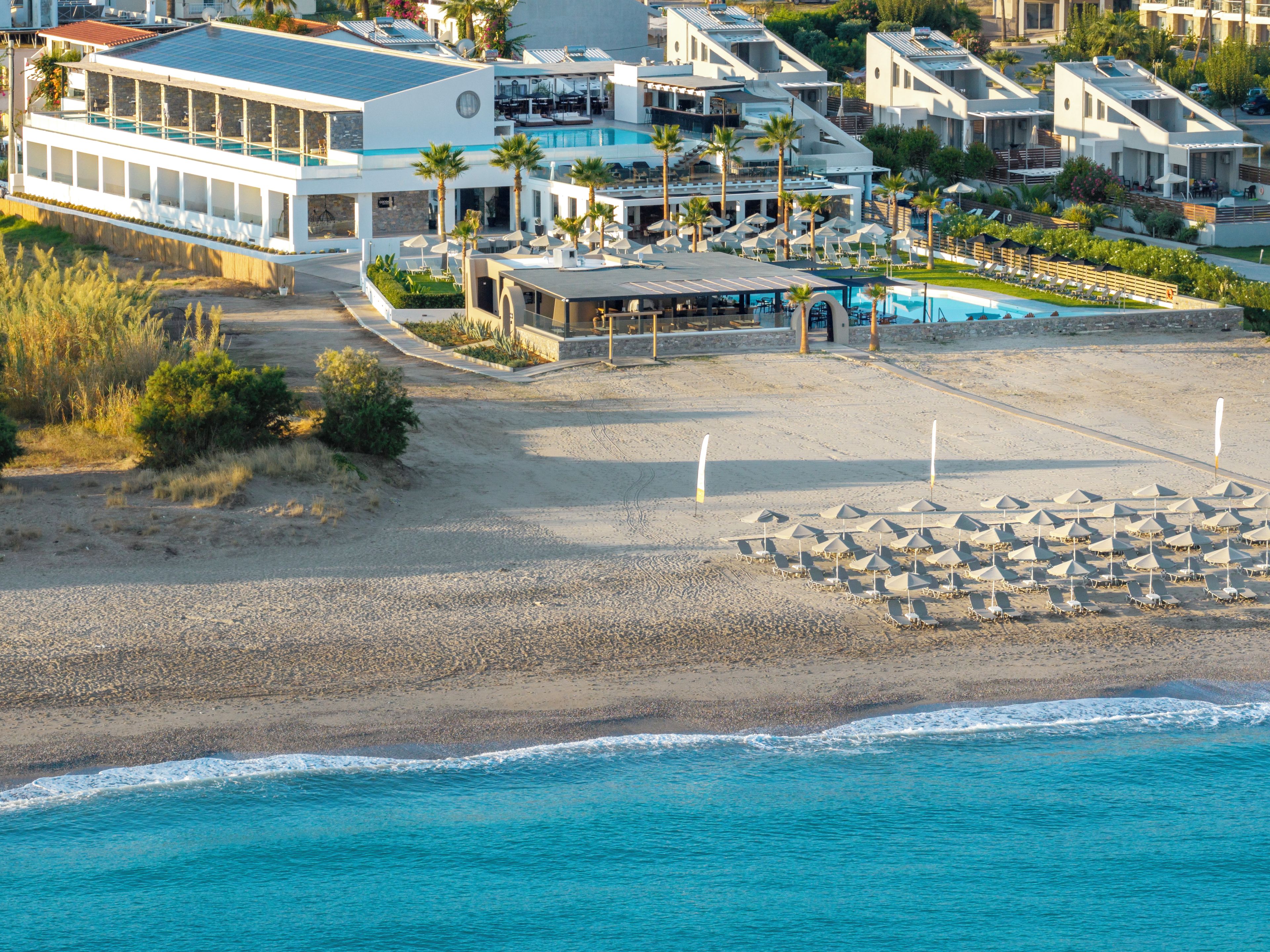 A beachfront property with a pool, multiple buildings, and a sandy beach.