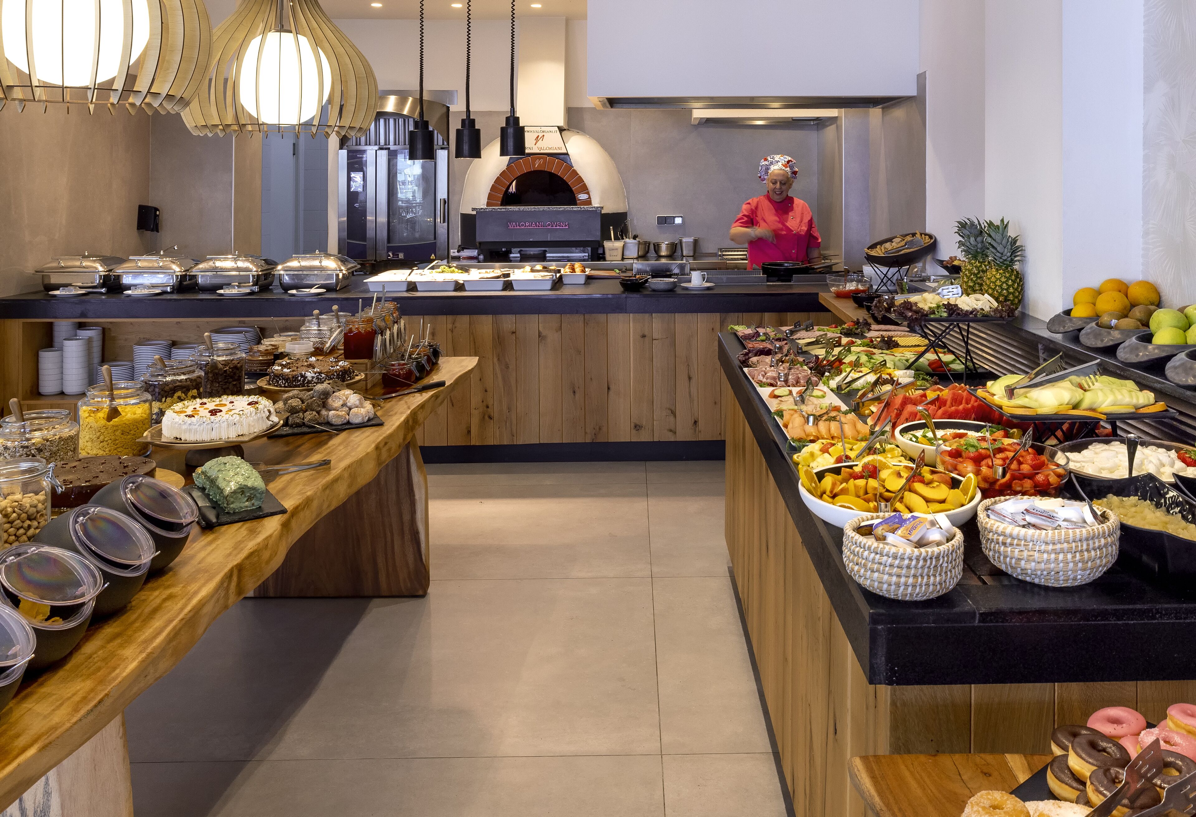 A buffet with various food items, a pizza oven, and a chef preparing food.