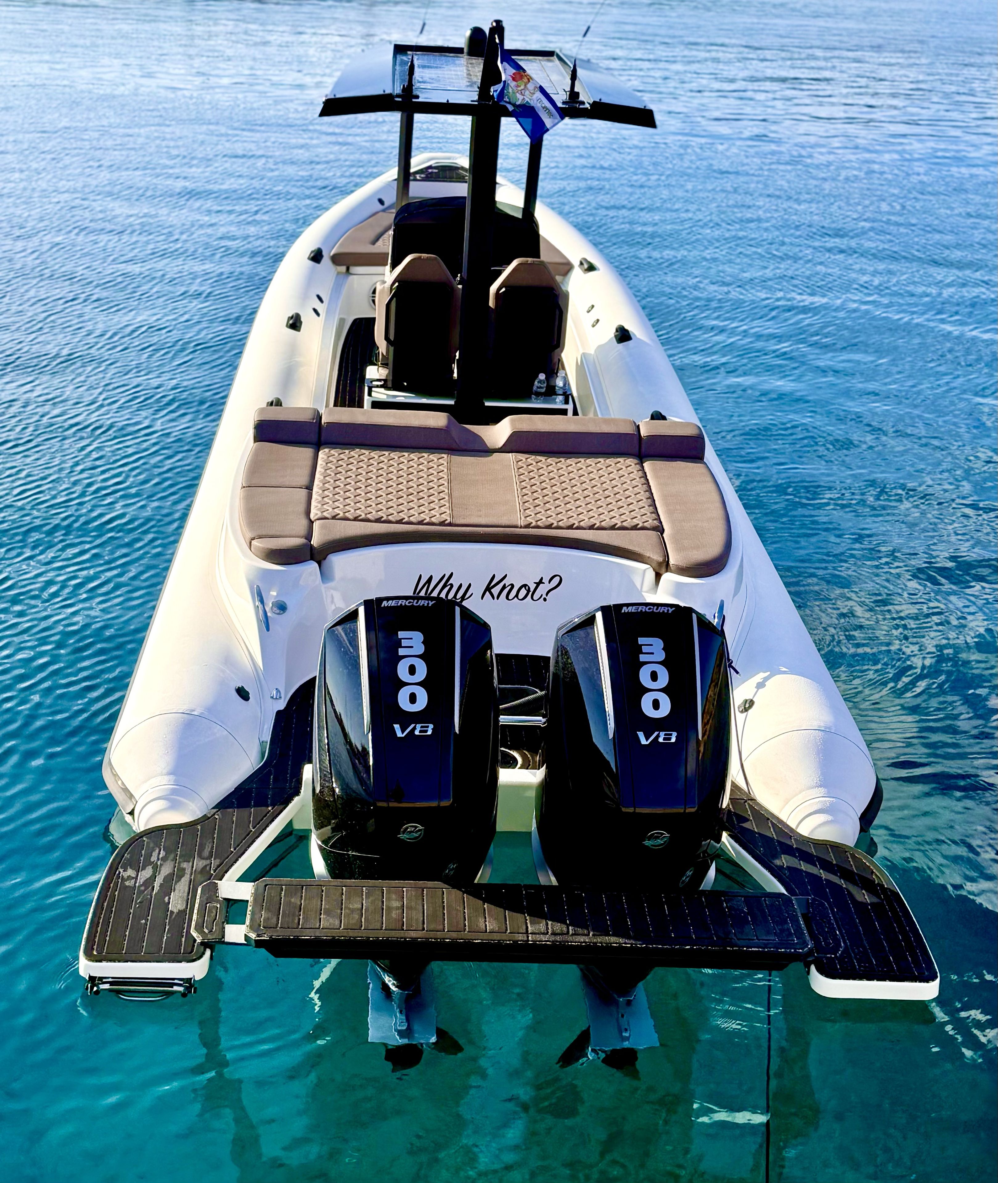 A boat with two Mercury V8 engines, a seating area with cushions, and a "Why Knot?" sign.