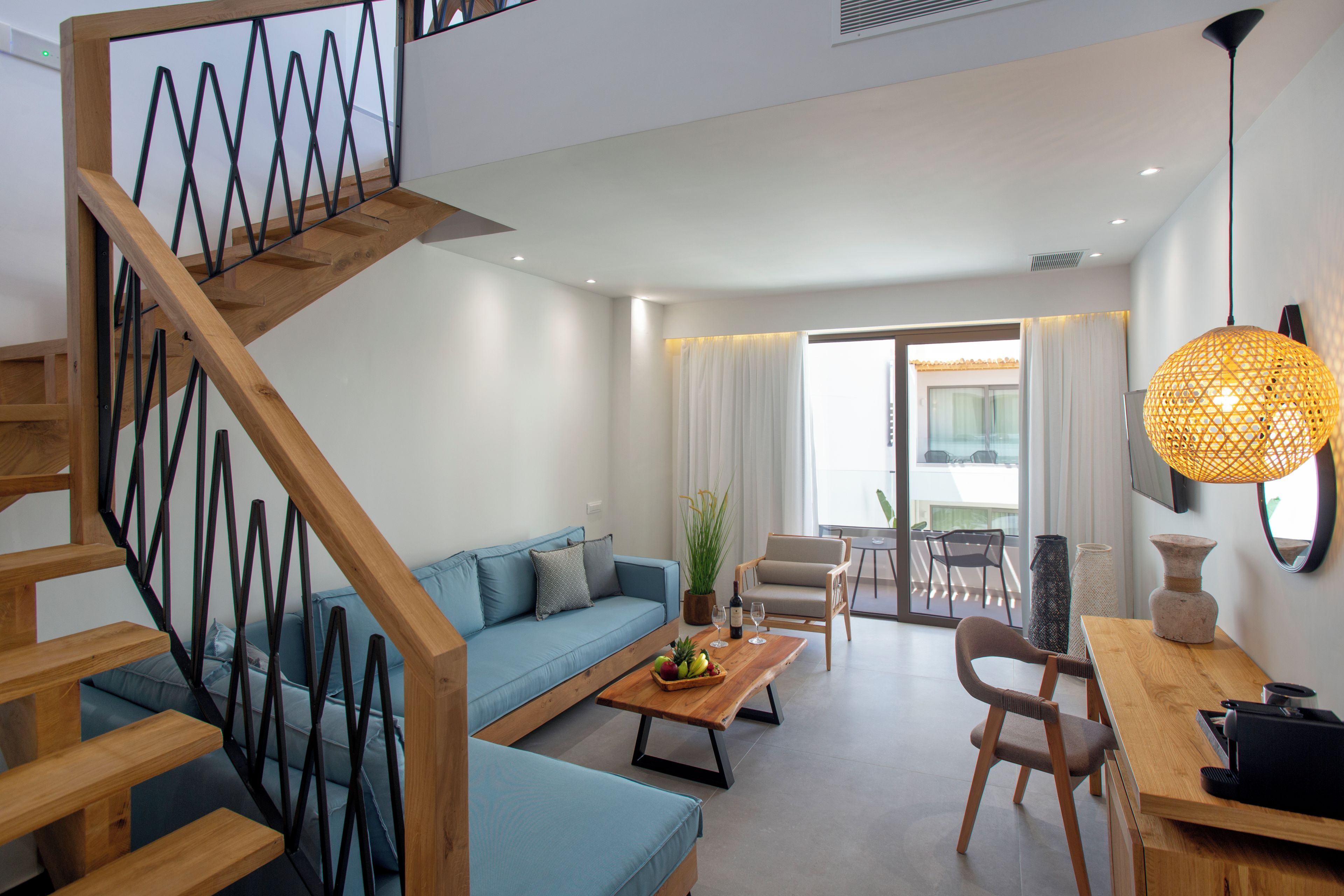 A modern living room with a staircase, a sofa, a coffee table with fruit, and a dining area with chairs and a table.