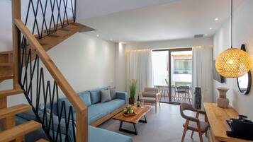 A modern living room with a staircase, a sofa, a coffee table with fruit, and a dining area with chairs and a table.