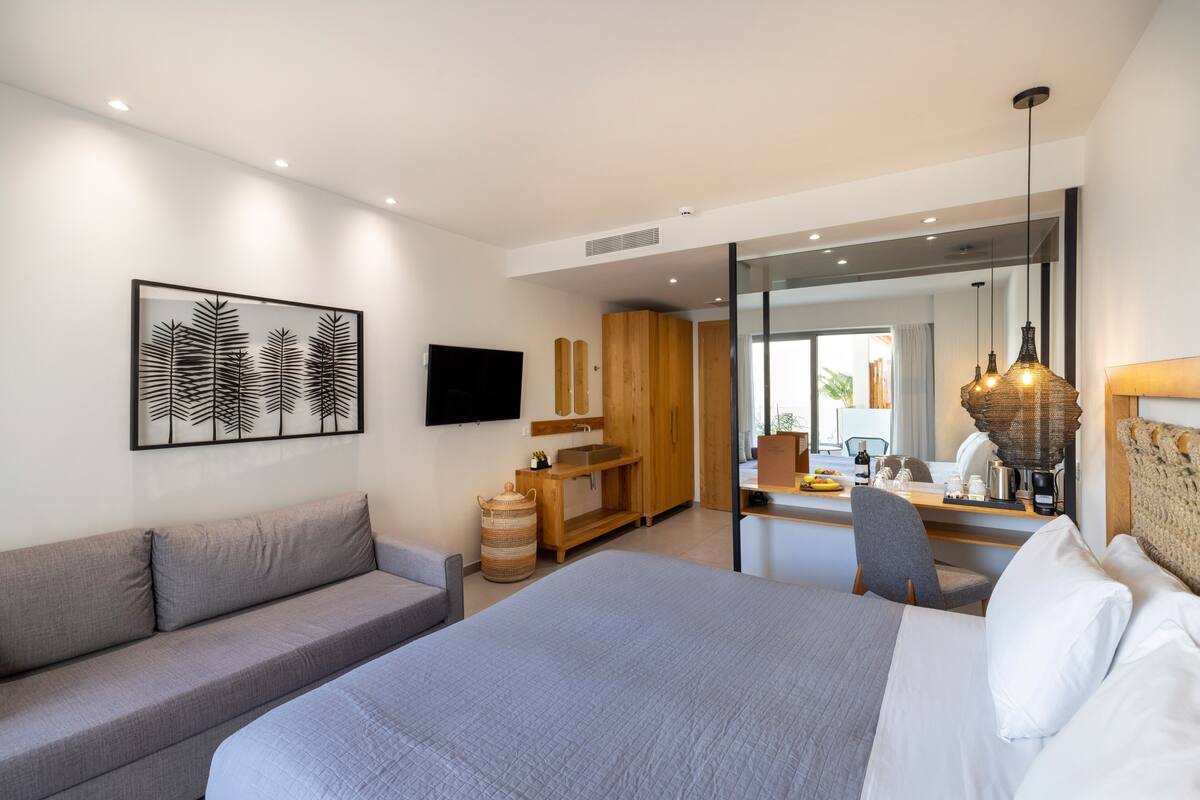 Una habitación de hotel moderna con una cama grande, un sofá, un armario de madera y un televisor.