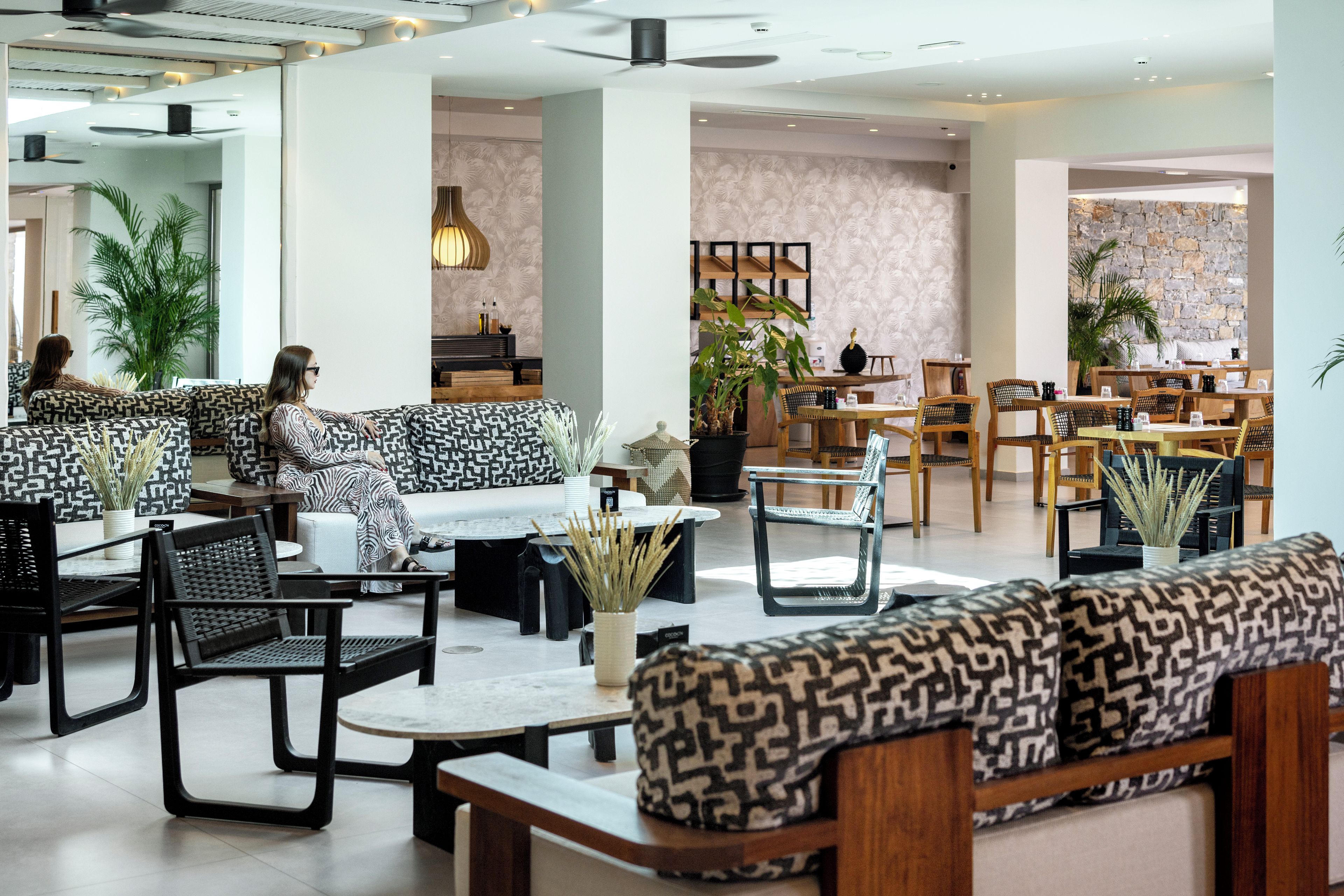A modern hotel lobby with seating areas, tables, and plants.