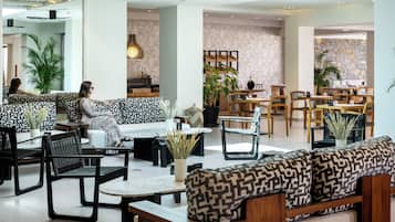 A modern hotel lobby with seating areas, tables, and plants.