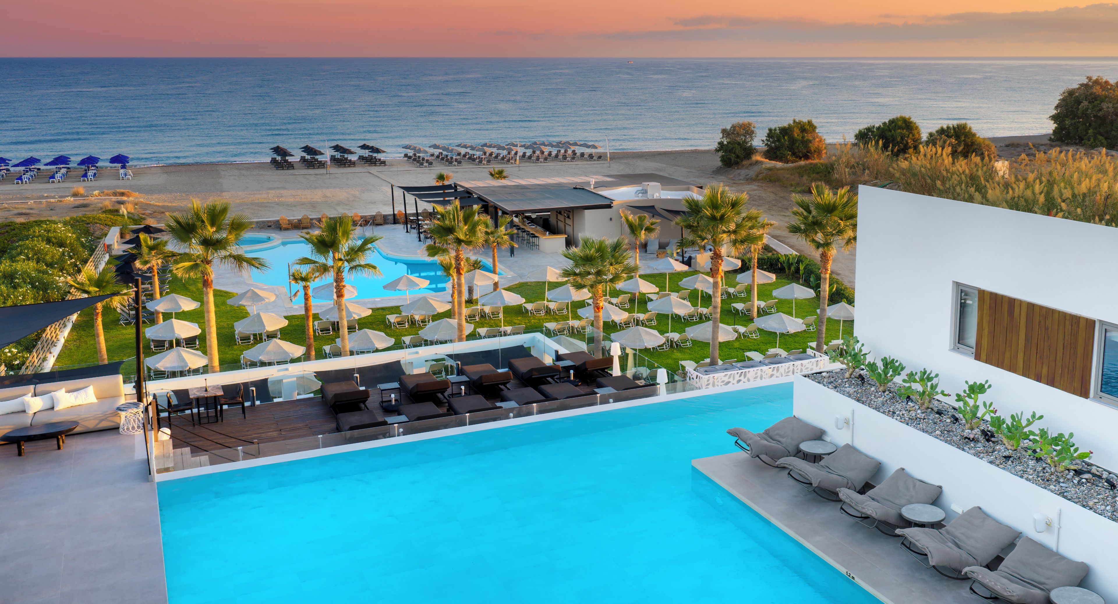 A pool area with lounge chairs and umbrellas, a beach with umbrellas and lounge chairs, and a view of the ocean.