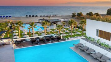 A pool area with lounge chairs and umbrellas, a beach with umbrellas and lounge chairs, and a view of the ocean.