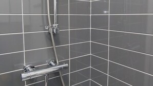 A shower with a chrome hose and control knobs, set in a room with grey tiled walls. - Townhouse @166 Ruskin Rd (Crewe)