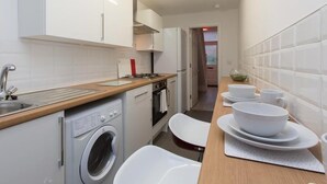 A modern kitchen with white cabinetry, a stainless steel sink, a built-in washing machine, and a wooden countertop. - Townhouse @166 Ruskin Rd (Crewe)