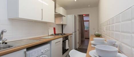 Cocina moderna con armarios blancos, pileta de acero inoxidable, lavadora integrada y encimera de madera.