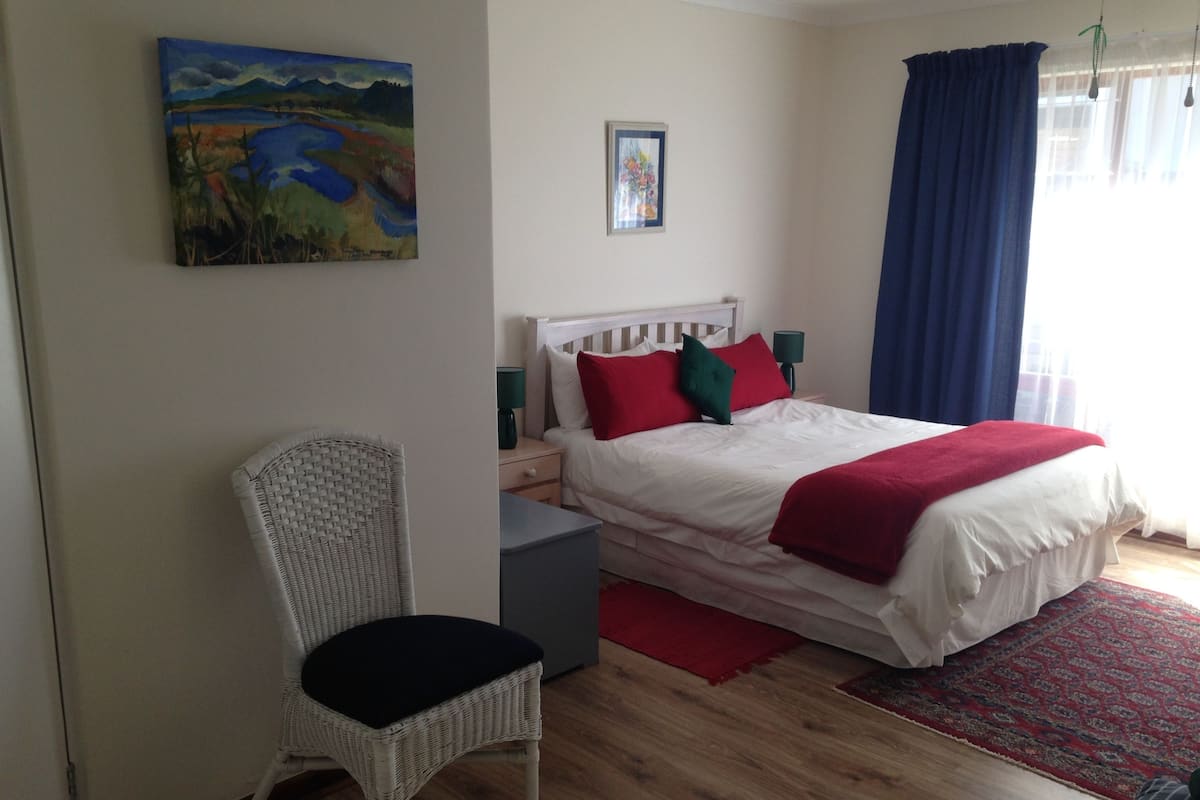 Une chambre à coucher avec un lit, une chaise, une table de chevet, une lampe et un tableau au mur.