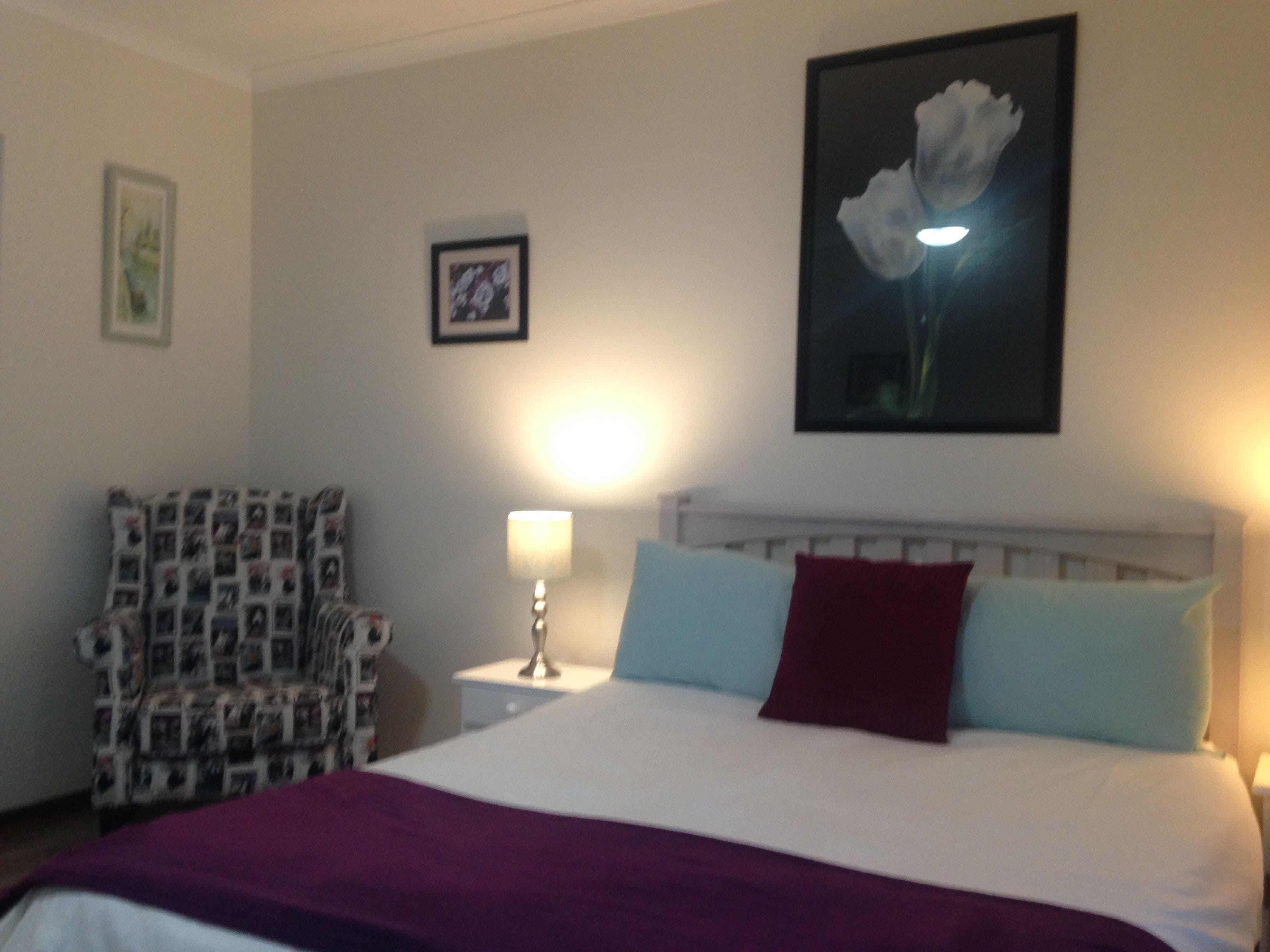 Een slaapkamer met een bed, een stoel, een nachtkastje en een aan de muur hangend schilderij.
