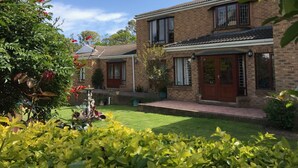 A two-story brick house with a well-maintained garden, a fountain, and a clear blue sky. - Blue Fern of Knysna (Knysna)