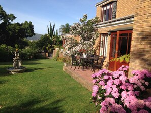A well-maintained garden with a fountain, a patio table with chairs, and blooming flowers.