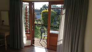 A room with a bed, a desk, and a view of a garden through an open door. - Blue Fern of Knysna (Knysna)