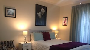 A bedroom with a bed, two bedside tables, a nightstand, a patterned armchair, and a rug. - Blue Fern of Knysna (Knysna)