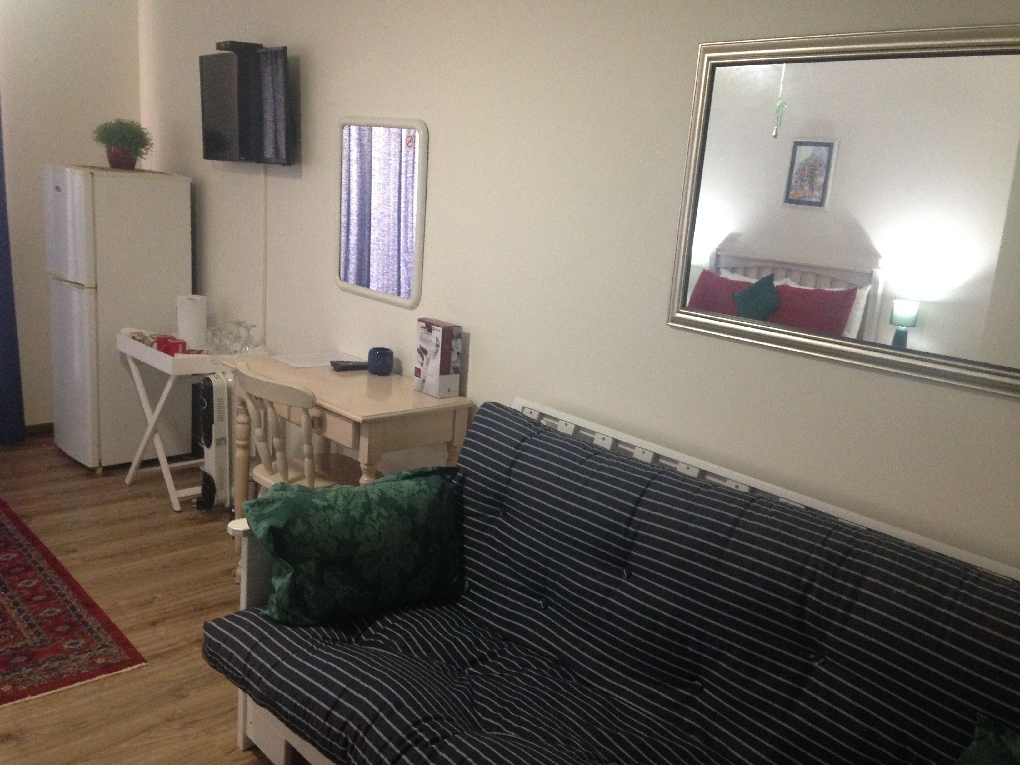 A compact living space with a sofa, a small desk, a mirror, and a refrigerator.