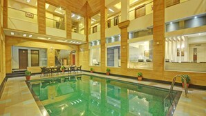 Una piscina interior con suelo de baldosas, paneles de madera y una zona de estar con mesas y sillas.