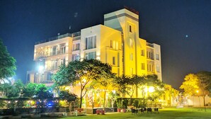 Un hotel de varios pisos con un patio central, mobiliario exterior e iluminación destacada en la fachada.