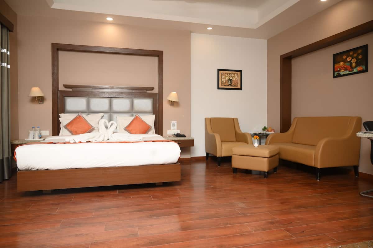 Una habitación de hotel con una cama grande, dos sillones, una mesita y un cuadro en la pared.