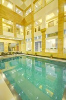 Una piscina cubierta de varios niveles con agua cristalina, paneles de madera y una zona de estar con mesas y sillas.