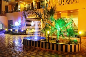 Un patio con una fuente, palmeras y un edificio con balcones.