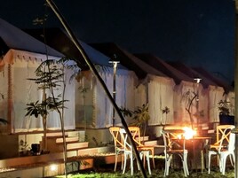 Un espacio al aire libre con carpas, sillas y mesas blancas, rodeado de plantas y una escalera que conduce a la entrada de la carpa.