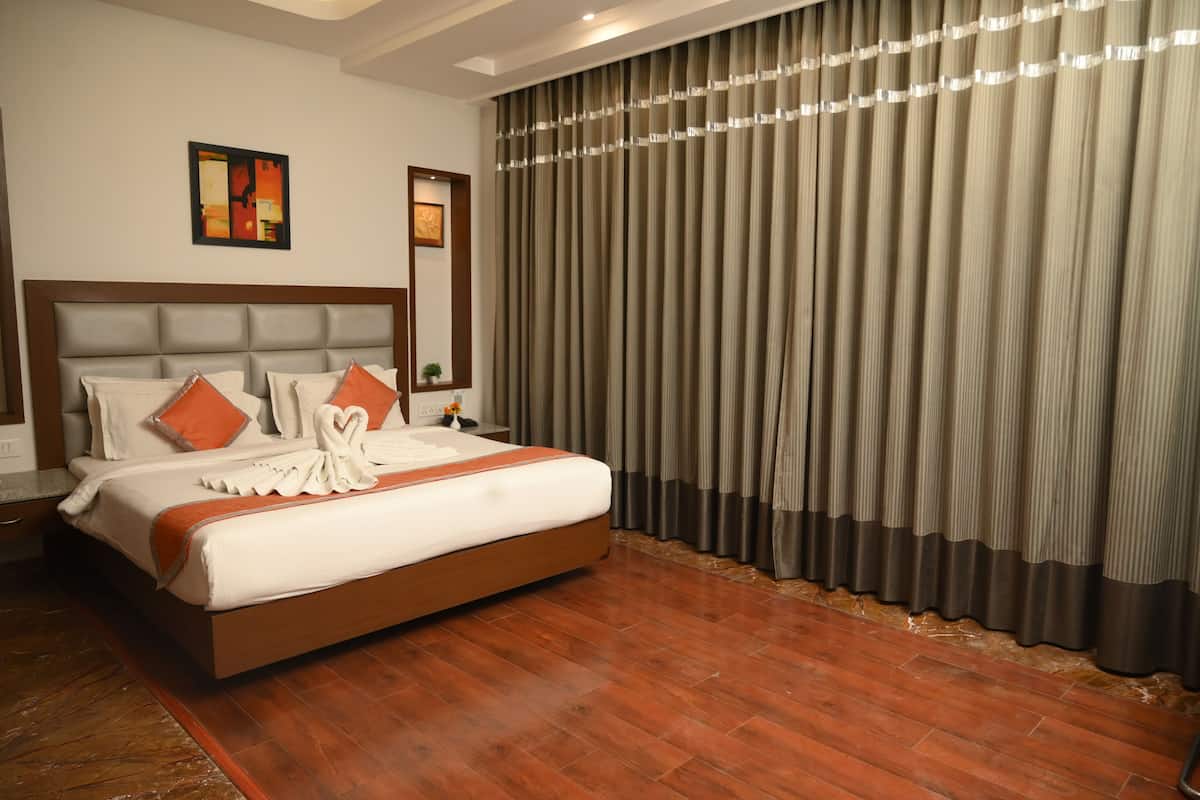 Habitación de hotel con una cama grande, cabecero de madera y vista a una ventana cubierta por cortinas.