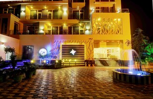 Un hotel de varios pisos con una entrada bien iluminada, una fuente y el letrero del hotel Zinc.