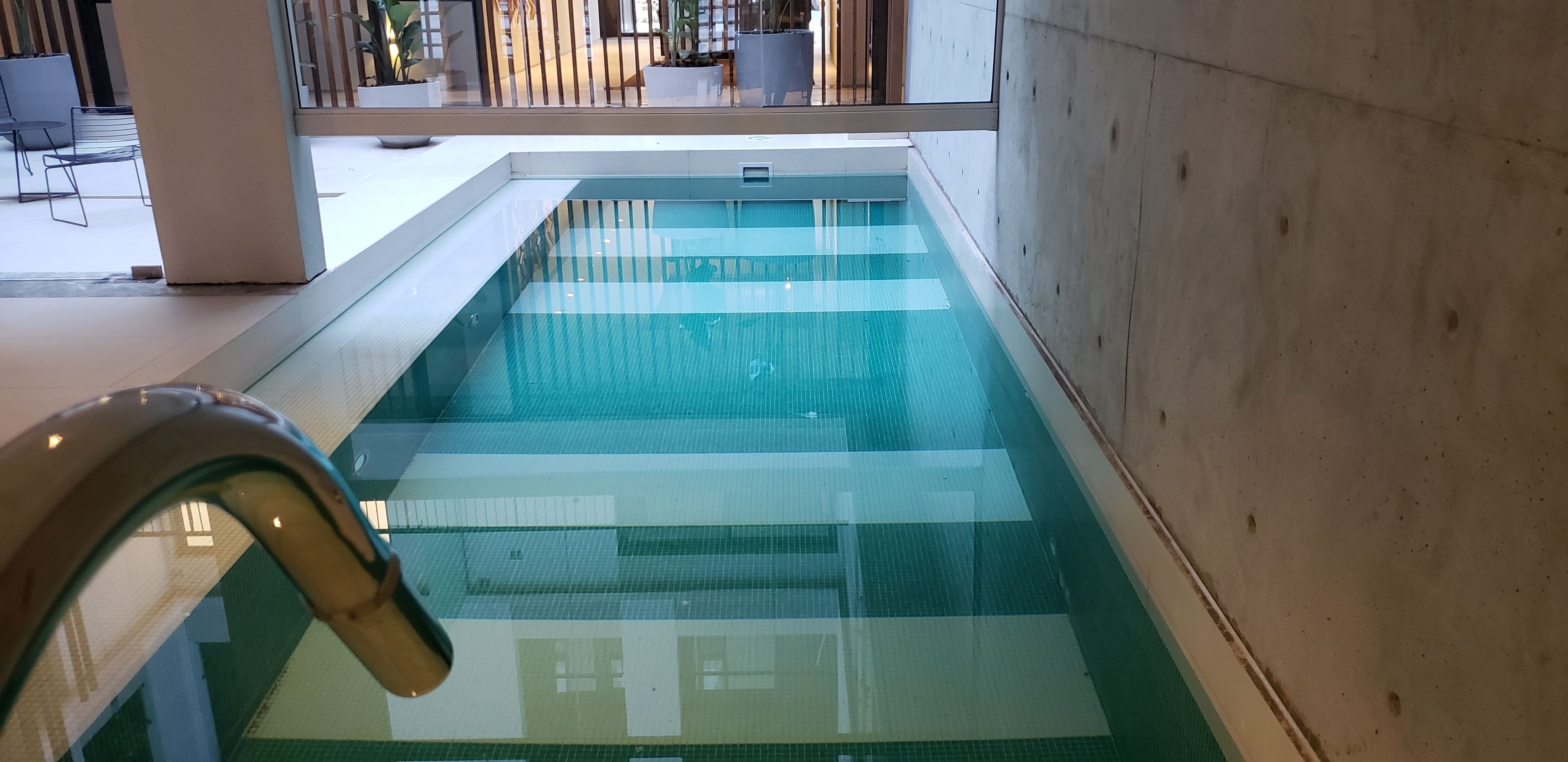 Une piscine intérieure à l’eau claire, entourée d’un mur en béton et d’une barrière en verre.