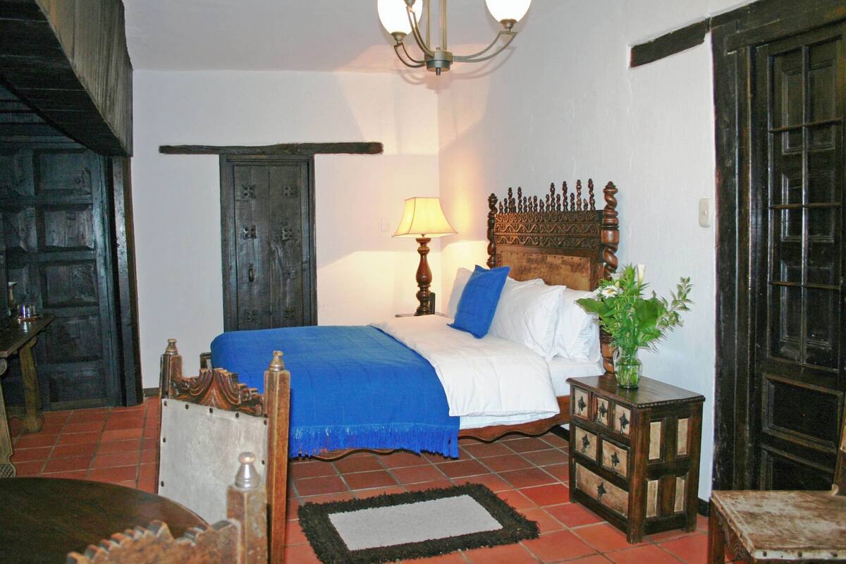 Un dormitorio tradicional con una cama de madera, una mesita de noche, una lámpara y una planta en maceta.