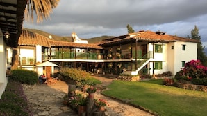 Un edificio grande de varios pisos con un patio, sendero de piedra y abundante vegetación.