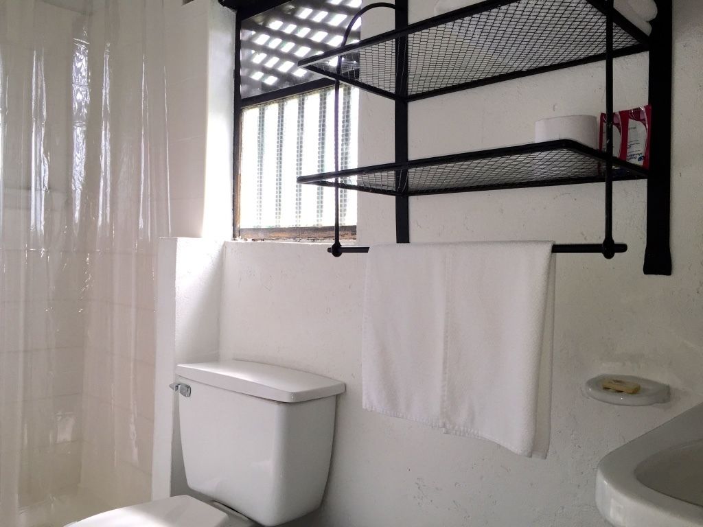 Une salle de bain avec des toilettes blanches, un lavabo blanc et une étagère en métal noir au-dessus du lavabo.