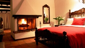 Un dormitorio con chimenea, una cama con colcha roja y un espejo en la pared.