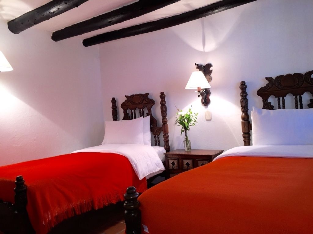 A room with two beds, each with a red bedspread, wooden headboards, and a small table with a lamp between them.