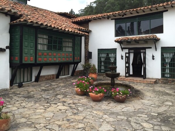 A courtyard with stone flooring, traditional buildings with green shutters, and potted plants. - Hotel San Luis De Ucuenga (Nobsa)