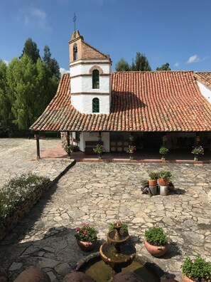 A traditional building with a tiled roof and a bell tower, surrounded by stone pathways and potted plants. - Hotel San Luis De Ucuenga (Nobsa)
