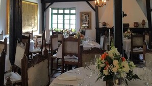 Un comedor con mesas redondas dispuestas para una comida, sillas de madera y un candelabro.