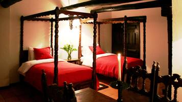 Ein traditionelles Himmelbett mit roter Bettwäsche, eine brennende Kerze, Holzmöbel und ein Fliesenboden.