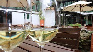 Dos copas de vino sobre una mesa de madera con asientos al aire libre, rodeado de sombrillas y plantas en macetas.
