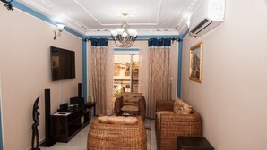 A living room with a TV, wicker furniture, and a view of the outside. - The Address Denver Residence (Douala)