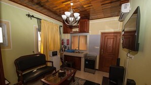 A compact living space with a sofa, a glass-top coffee table, a television, a kitchen area with a microwave, a stove, and a refrigerator. - The Address Denver Residence (Douala)