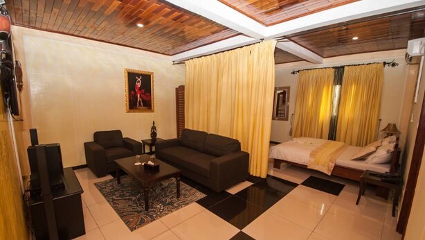 A hotel room with a sofa, a bed, a TV, and a ceiling with wooden beams. - The Address Denver Residence (Douala)