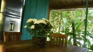 Un tavolo in legno rustico con un cesto intrecciato pieno di fiori bianchi, un elettrodomestico in acciaio inox e una sedia di legno.