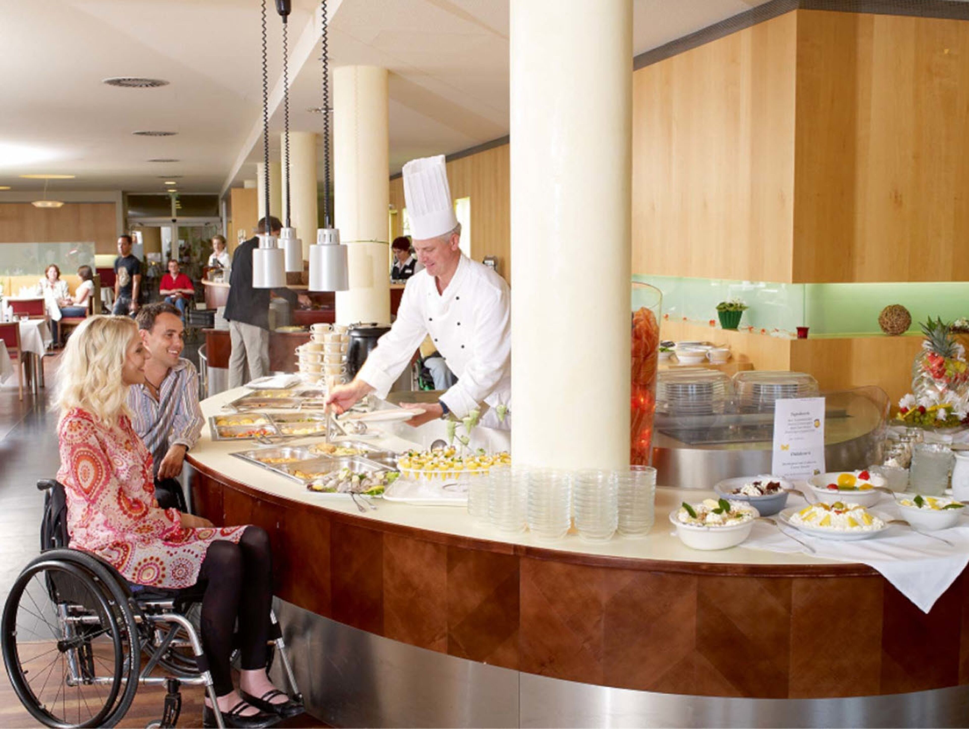 A buffet area with a chef serving food, a counter with various dishes, and a wheelchair-accessible seating area.