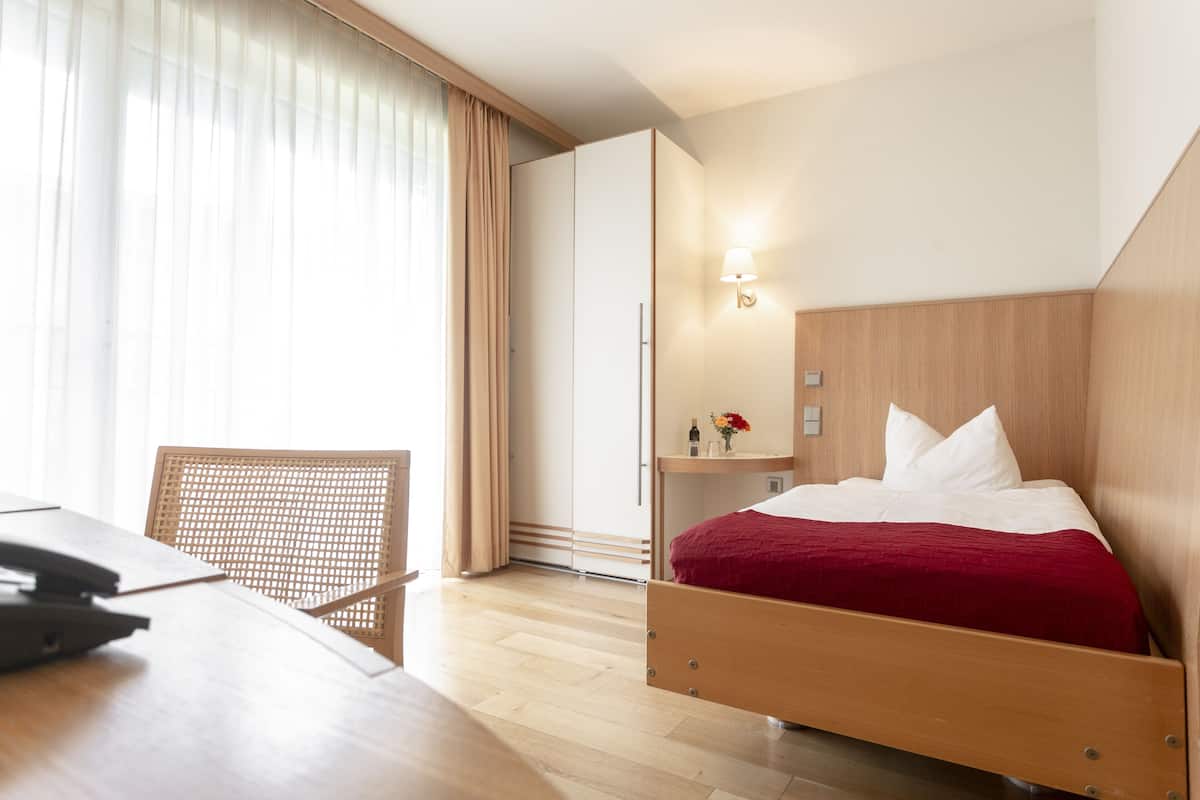 A hotel room with a wooden bed, a desk, a chair, and a nightstand with a lamp.