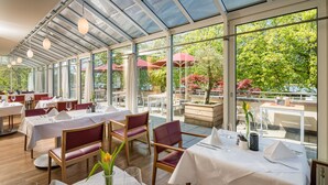 Ein Restaurant mit gedeckten Tischen, großen Fenstern und einer Terrasse mit Sonnenschirmen.