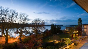Blick auf einen See mit einer Terrasse, Bäumen und einem Gebäude mit Balkon mit Seeblick.