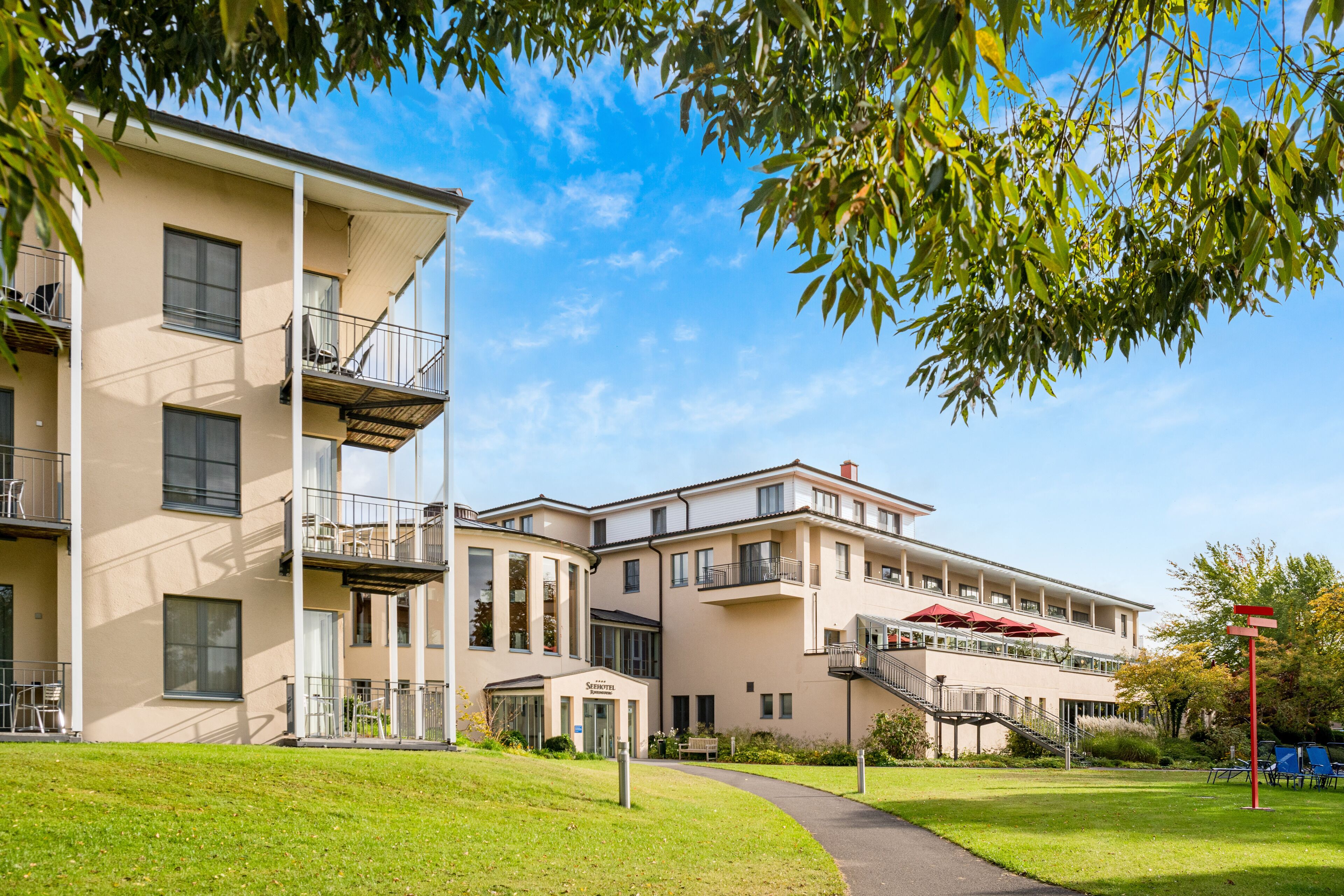 Um edifício residencial com vários andares, varandas, área externa coberta para sentar e um gramado bem cuidado.