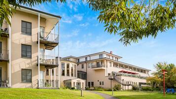 Um edifício residencial com vários andares, varandas, área externa coberta para sentar e um gramado bem cuidado.